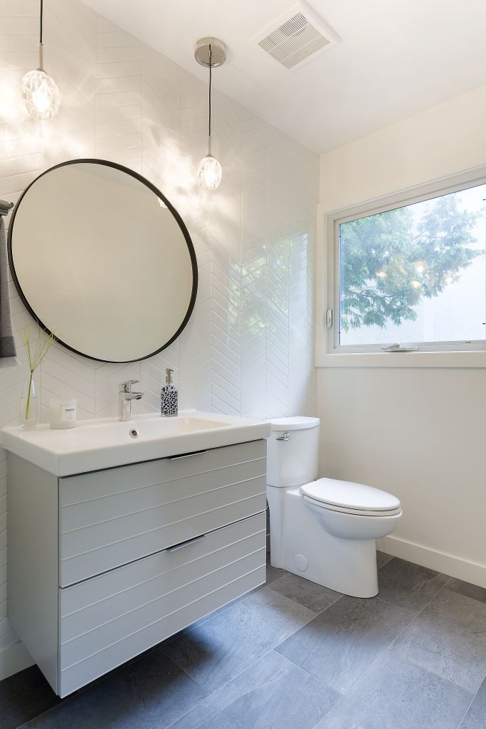 Modern bathroom with floating vanity, round mirror, and herringbone tile wall