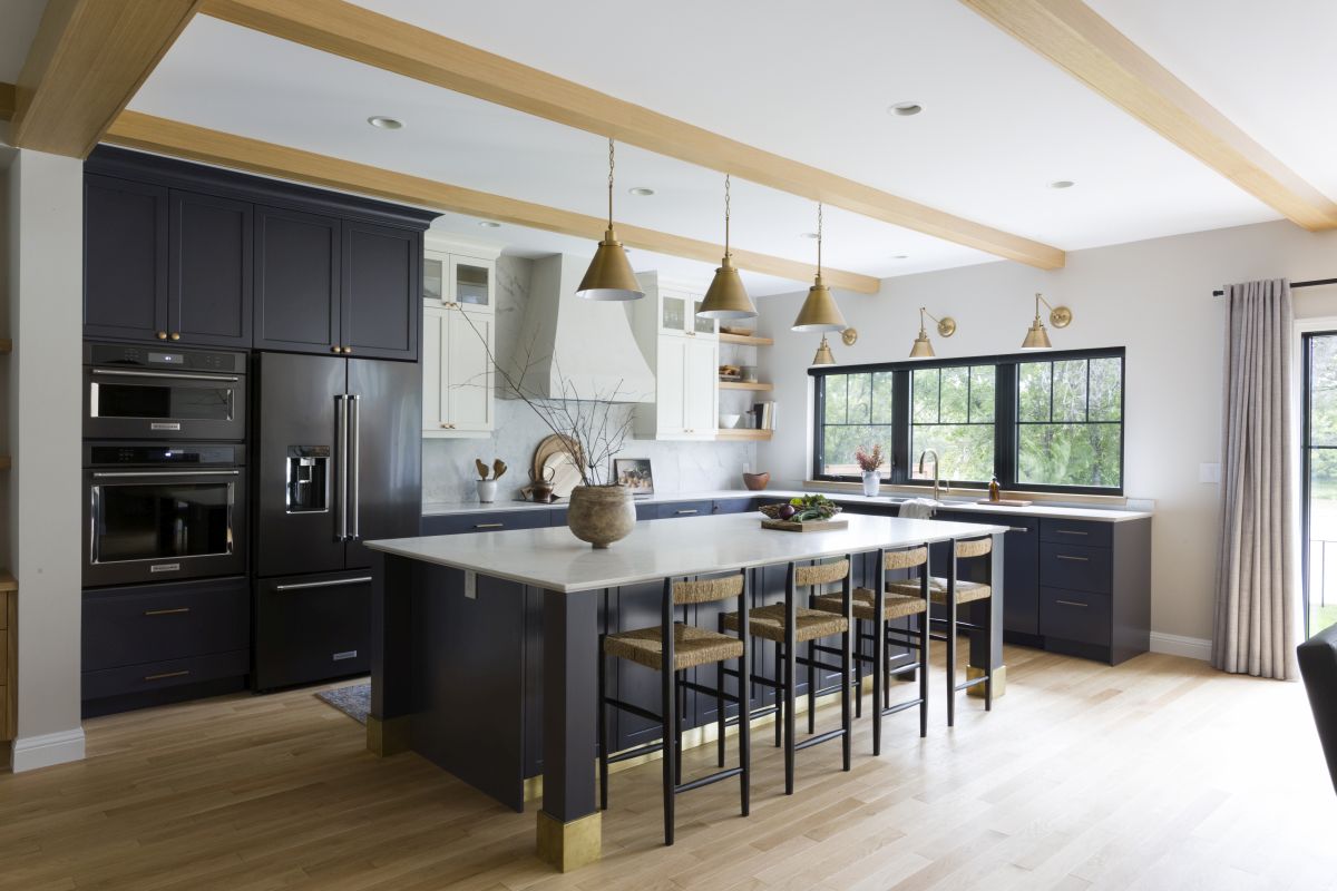 Modern kitchen with blue cabinets, white marble countertops, gold pendant lights, large island, and black-framed windows