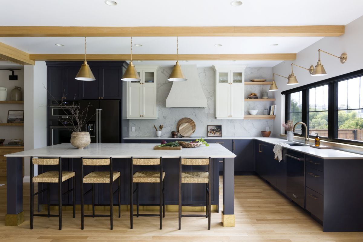Contemporary kitchen with blue cabinets, marble backsplash, gold lighting, large island, and black-framed windows