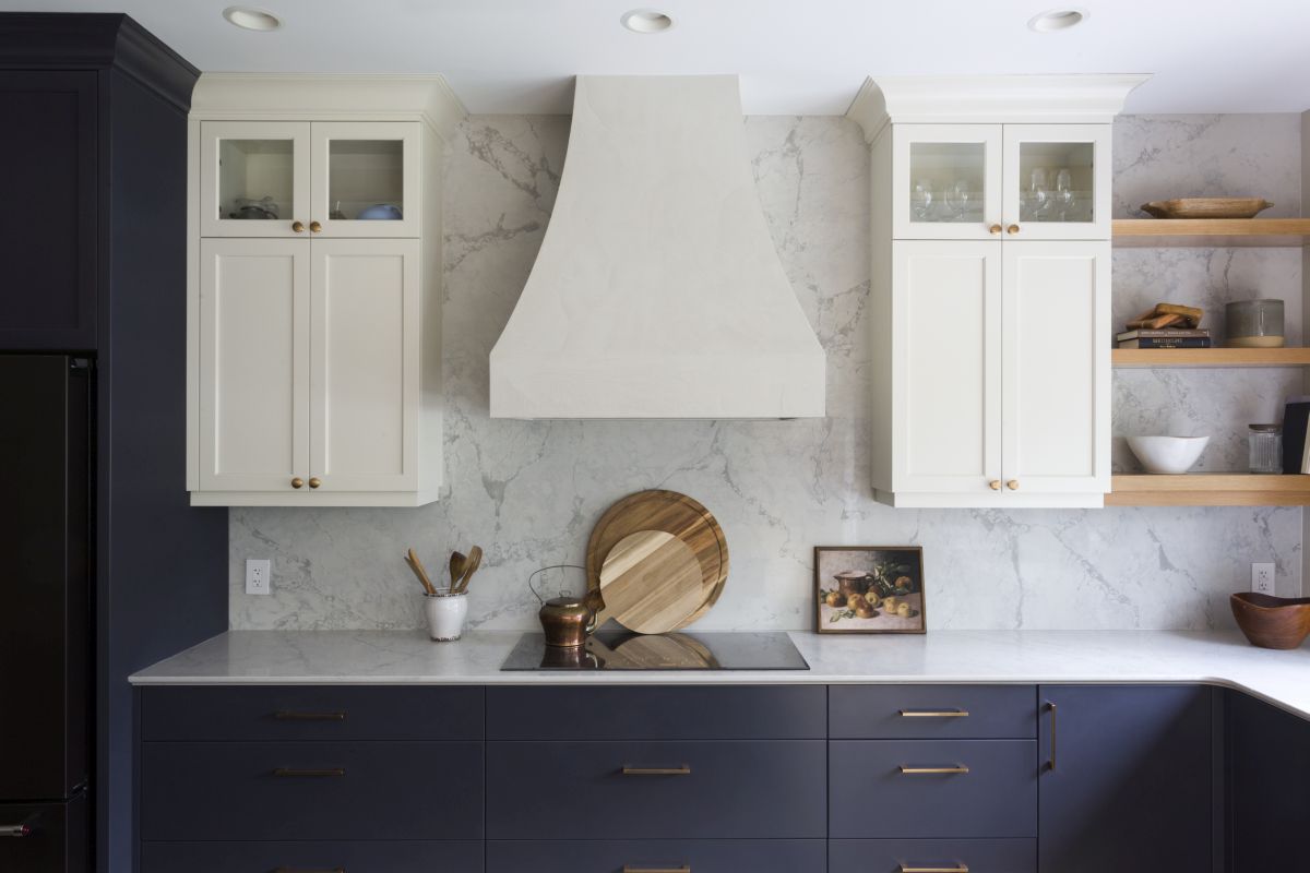 Modern kitchen with blue base cabinets, white wall cabinets, marble backsplash, and custom range hood