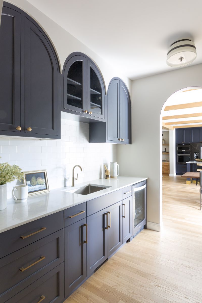 Custom kitchen cabinetry with navy blue arched cabinets, gold pulls,  white countertop, and white subway tile backsplash.