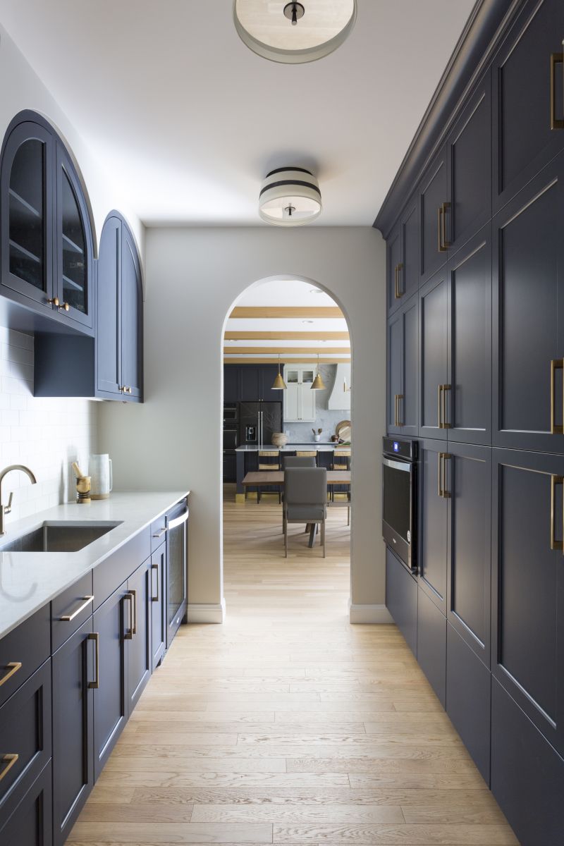Custom kitchen hallway with floor-to-ceiling cabinetry, shaker doors, white countertops, and arched entryway to main kitchen.