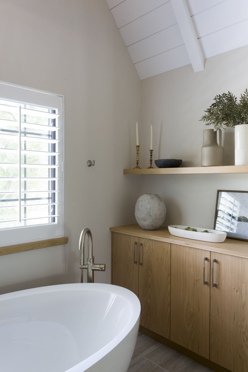 Minimalist bathroom design featuring freestanding tub, wood cabinets, and modern accents