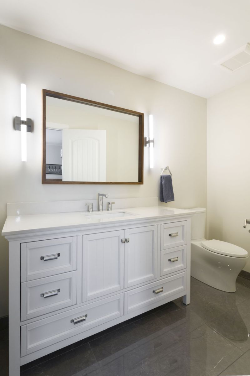 Elegant bathroom with clean white vanity, framed mirror, and polished gray tile floors