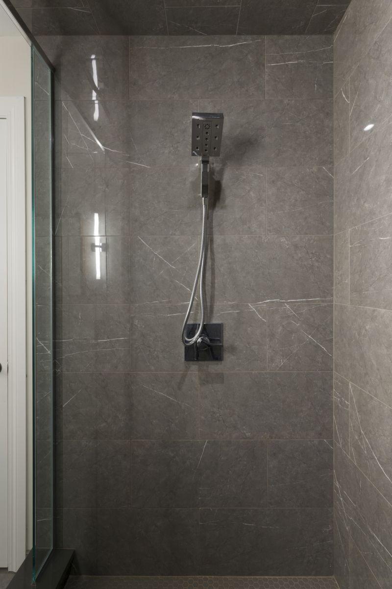 Minimalist shower design with polished gray tiles and a square rainfall showerhead with handheld attachment