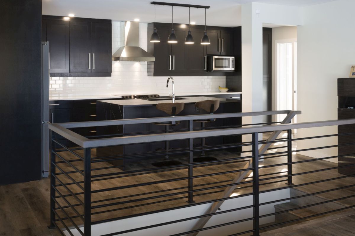 Bright, modern kitchen with glossy backsplash, black cabinets, and a staircase railing adding architectural detail