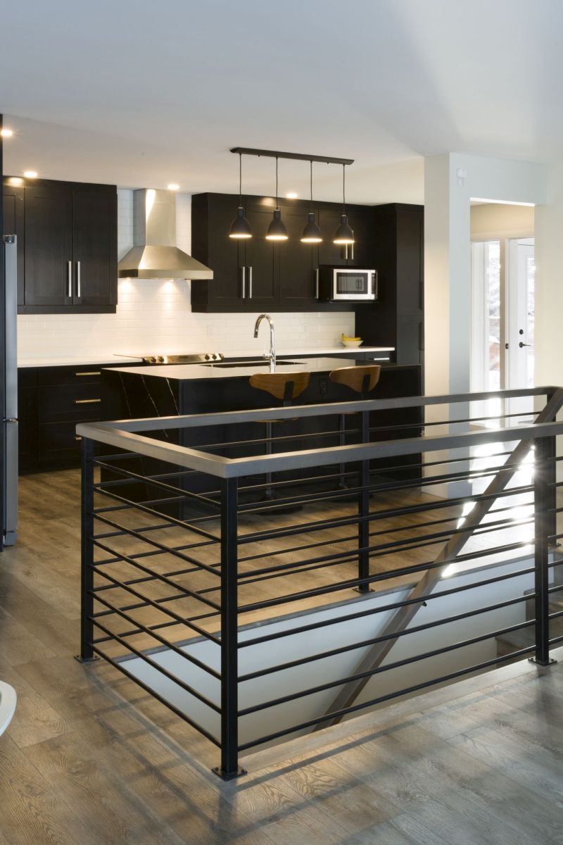 Modern kitchen with dark cabinetry, white subway tile backsplash, and black waterfall island countertop