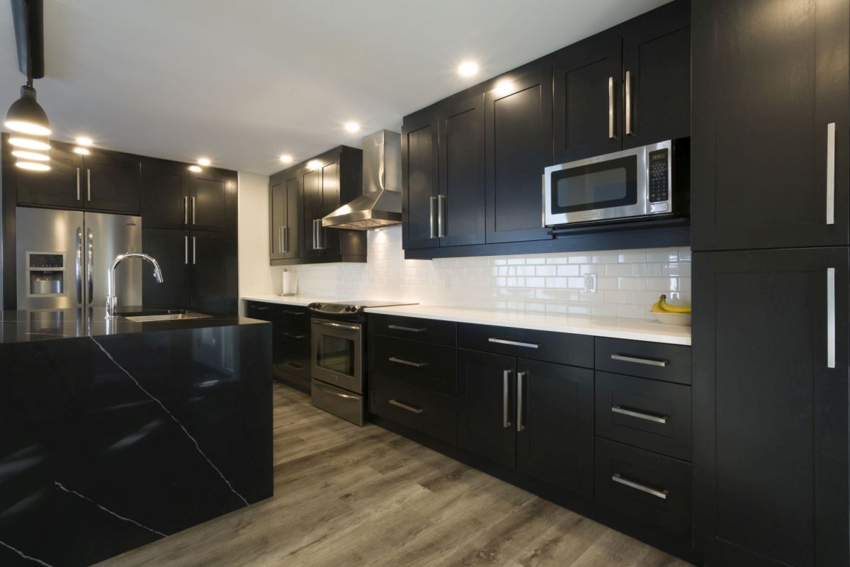 Minimalist kitchen with dark counters, black cabinetry, and a reflective white backsplash for contrast