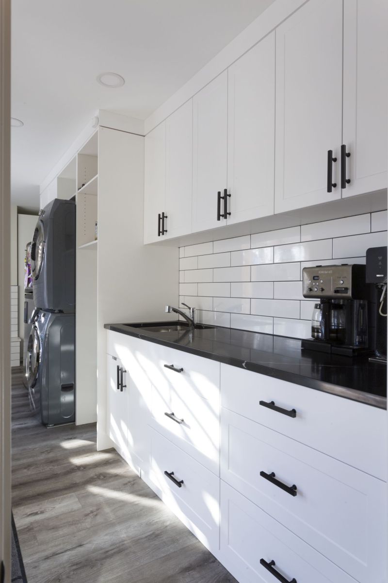 Bright laundry space featuring white shaker cabinets, black hardware, and subway tile backsplash