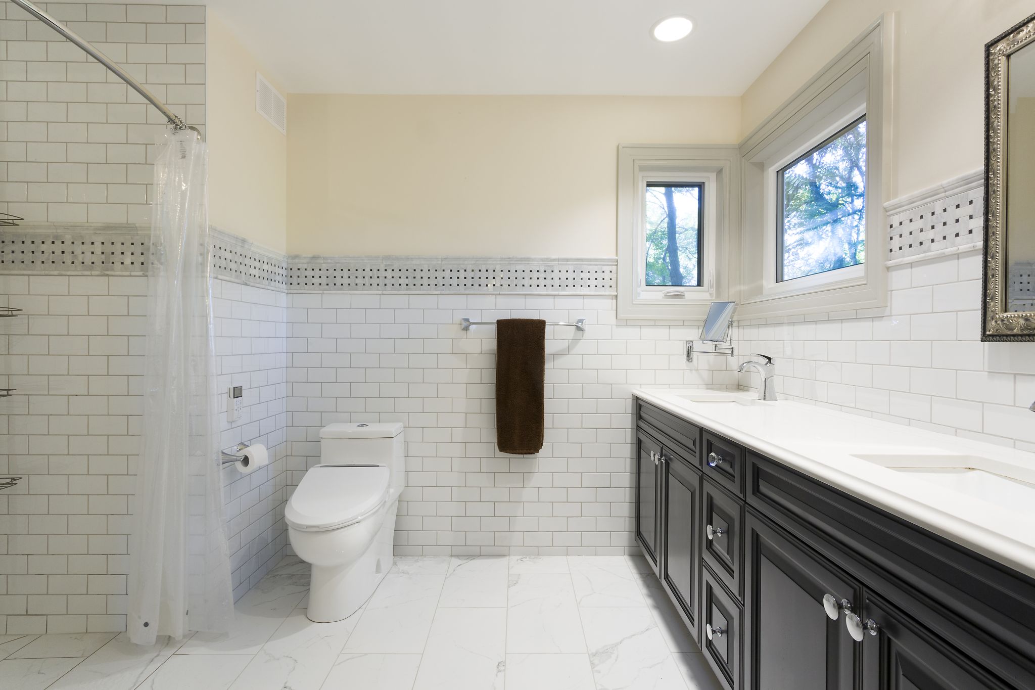 Elegant black vanity paired with subway tile wainscoting, mosaic detail, and marble-style tile floors.