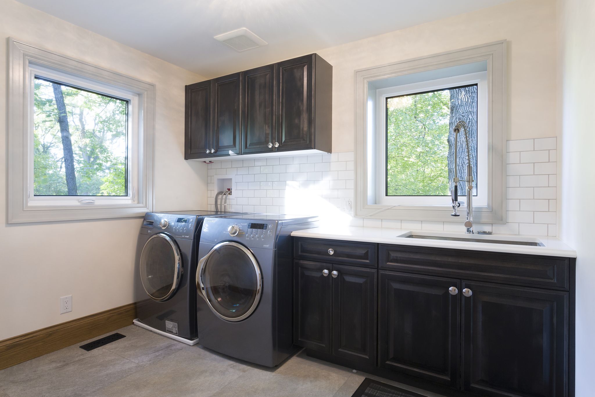 Contemporary laundry room with front load washer and dryer, black shaker cabinets, subway tile backsplash, and large windows