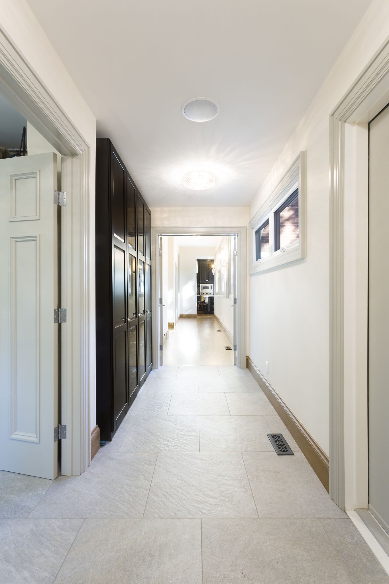 Bright hallway with neutral tile flooring, built-in black storage cabinets, and recessed ceiling lighting