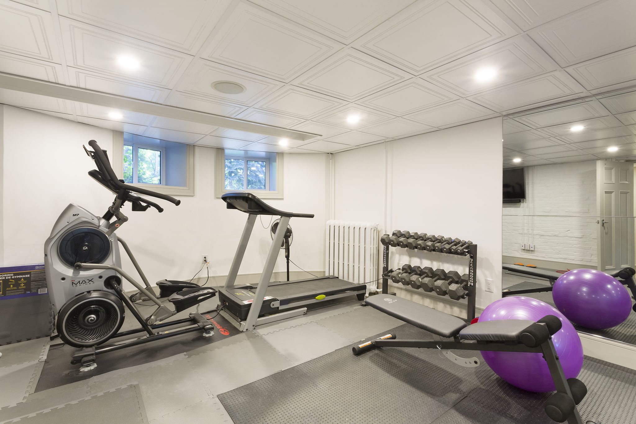 Basement home gym with exercise equipment, mirrored wall, recessed lighting, and white paneled ceiling